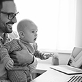 Man with a baby on his lap looking at a laptop screen